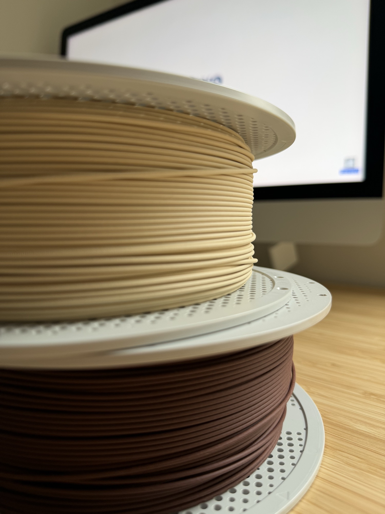 Two spools of 3D-printing filament, beige stacked on brown, on the workshop bench.