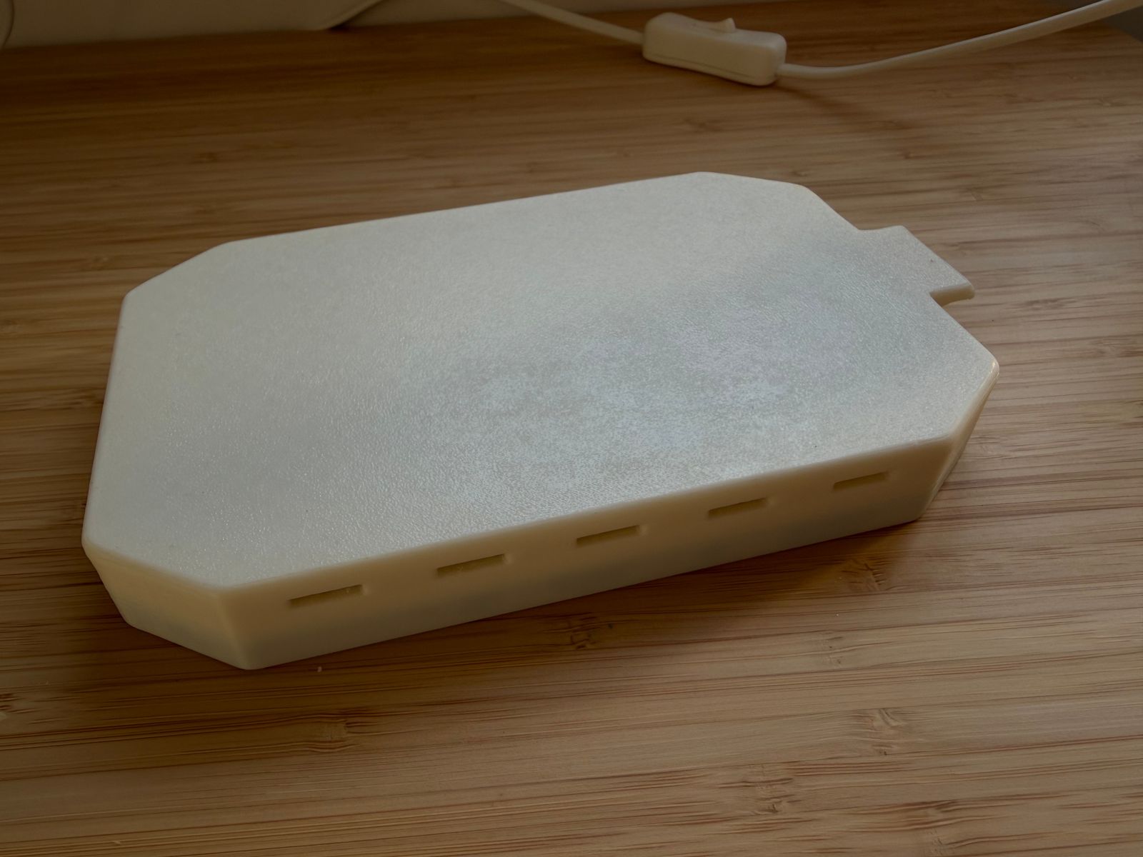 Side view of the white 3D-printed dash cover showing the row of ventilation slots along the skirt and the pull tab.