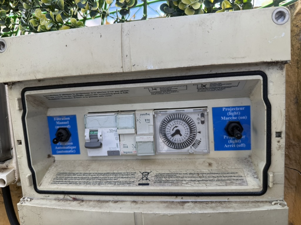 The outdoor pool control box with no front lid, its timer, breaker and switches exposed.
