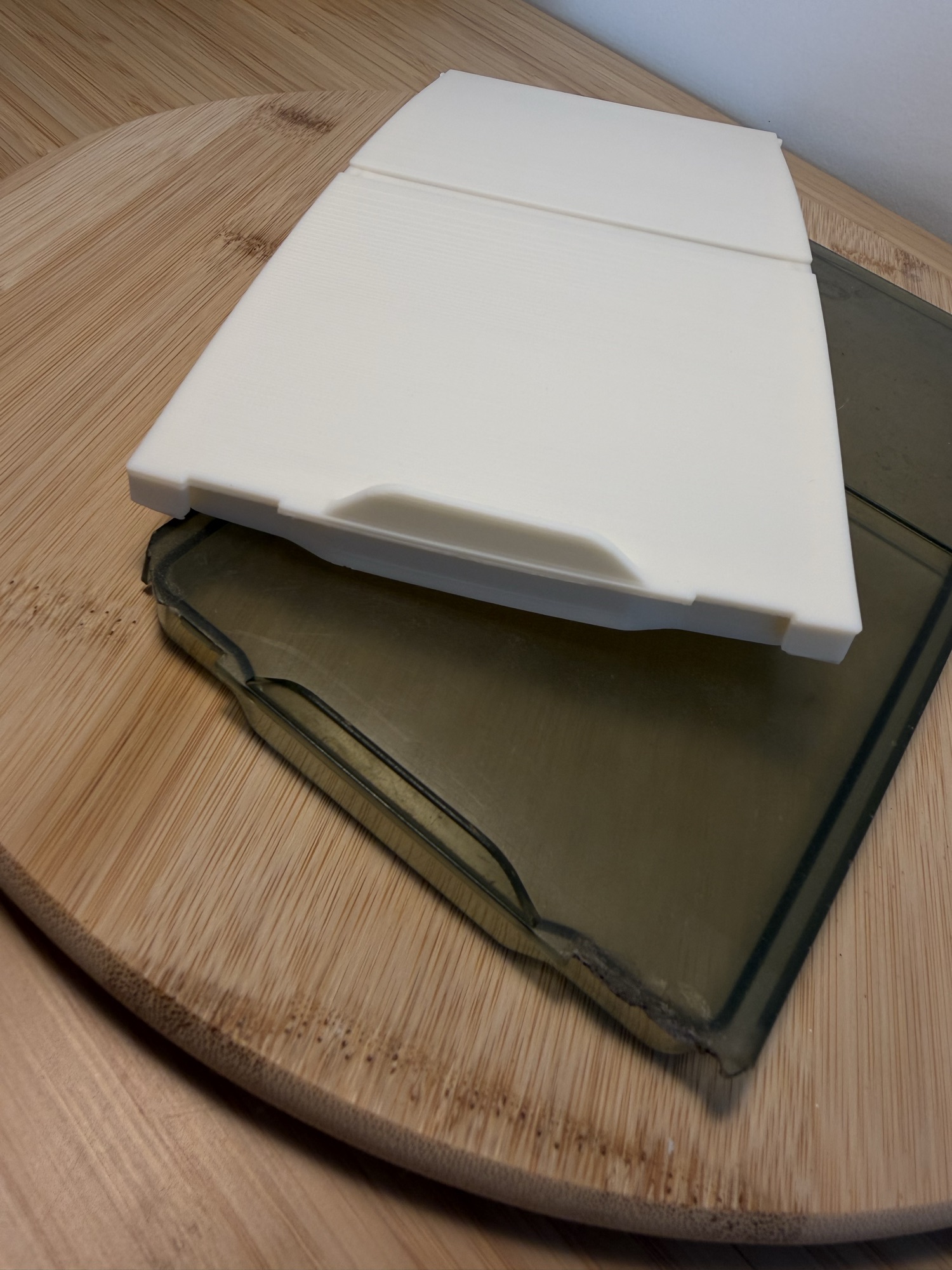 The new white 3D-printed lid propped over the cracked smoked-plastic original it replaces.
