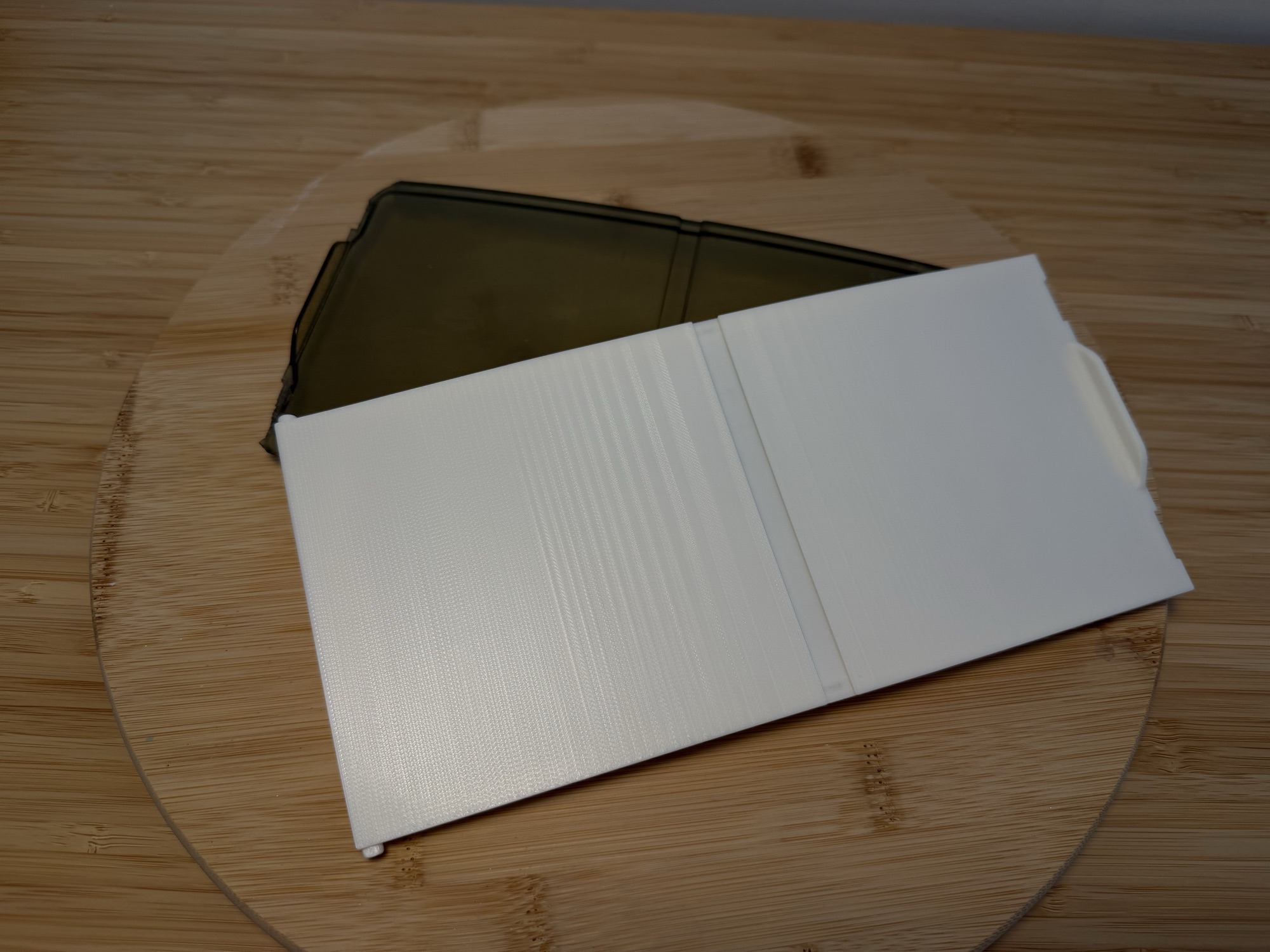 The new white lid lying across the original smoked plastic lid on a wooden board.