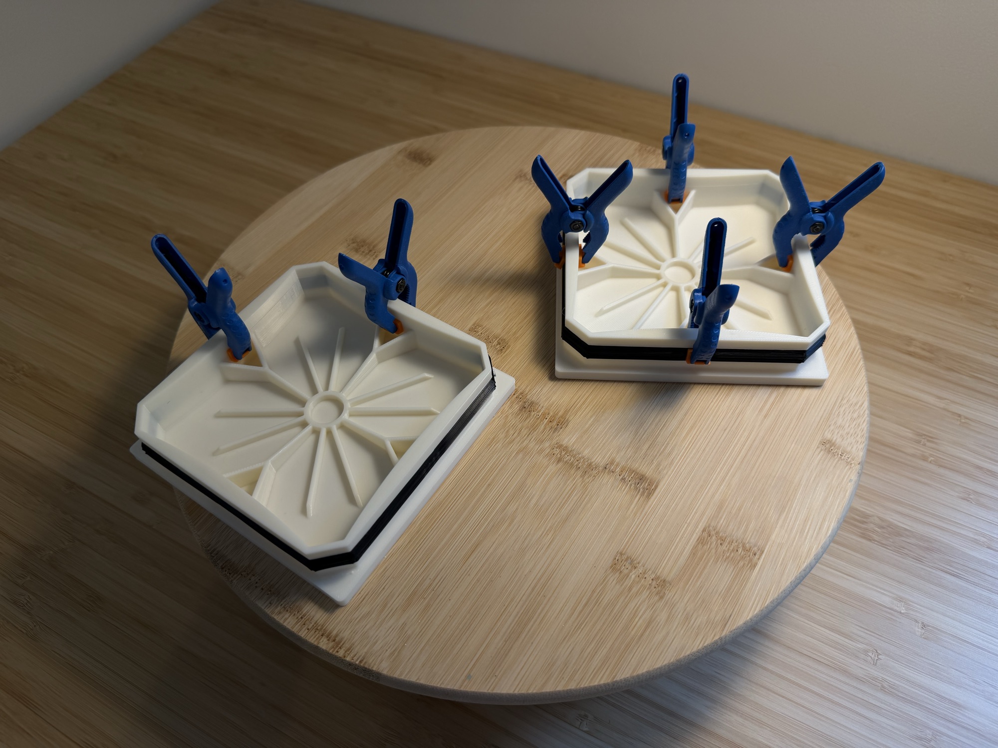 The two new caps on a wooden board, blue spring clamps holding each TPU gasket while the adhesive cures.